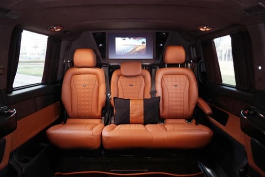 Cabine VIP de la Mercedes-Benz V250 Falcon Edition avec sièges capitaine en cuir matelassé fauve face à un écran de divertissement au plafond