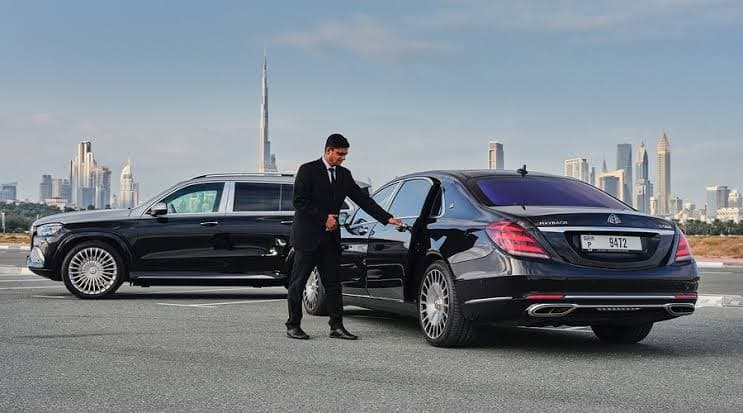 Chauffeur ouvrant la porte d'une Mercedes-Maybach Classe S à côté d'un SUV GLS avec la skyline de Dubaï en arrière-plan