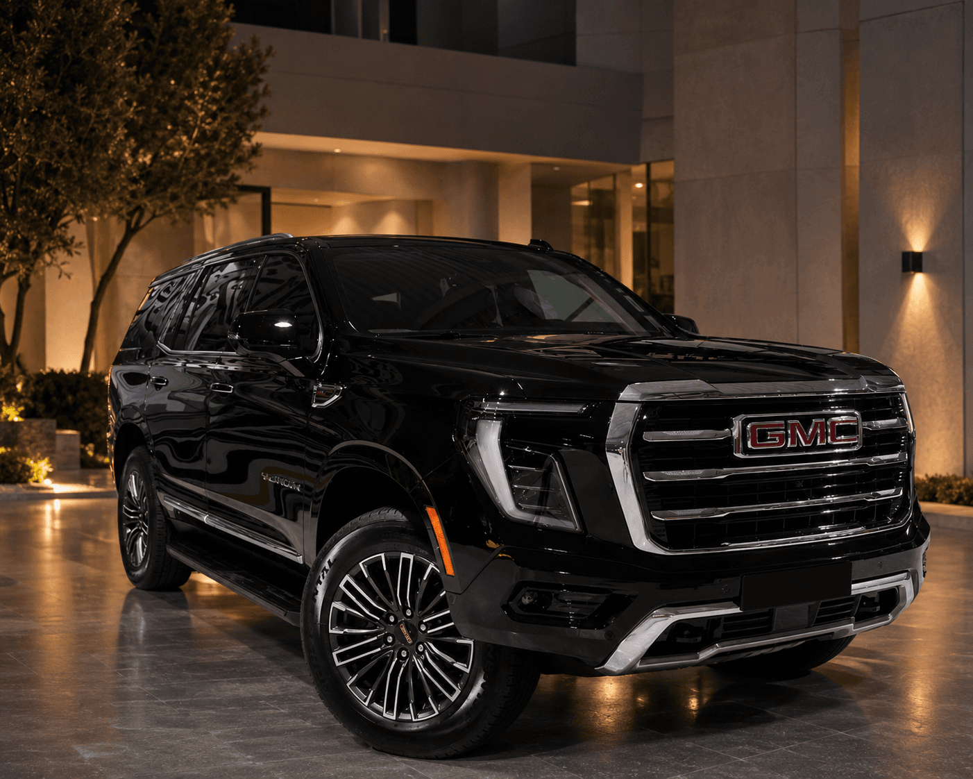 Вид спереди сбоку на GMC Yukon Elevation у современного освещённого входа ночью
