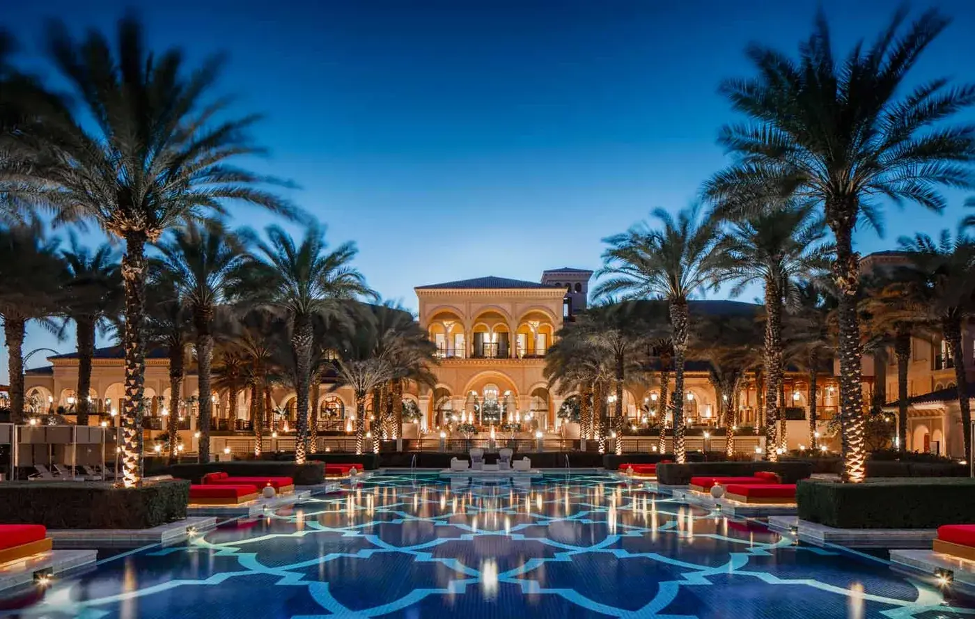 Luxury resort courtyard and pool lined with palm trees on Palm Jumeirah at dusk