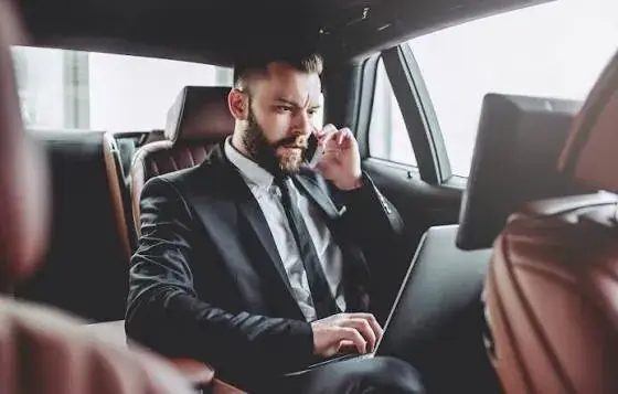 Businessman working on a laptop and taking a call in the back seat of an Apex Limo chauffeur car