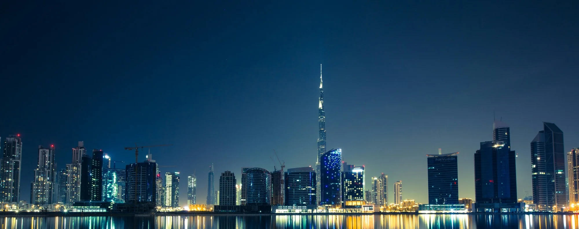 Skyline panoramique nocturne de Downtown Dubai avec le Burj Khalifa illuminé au-dessus du front de mer