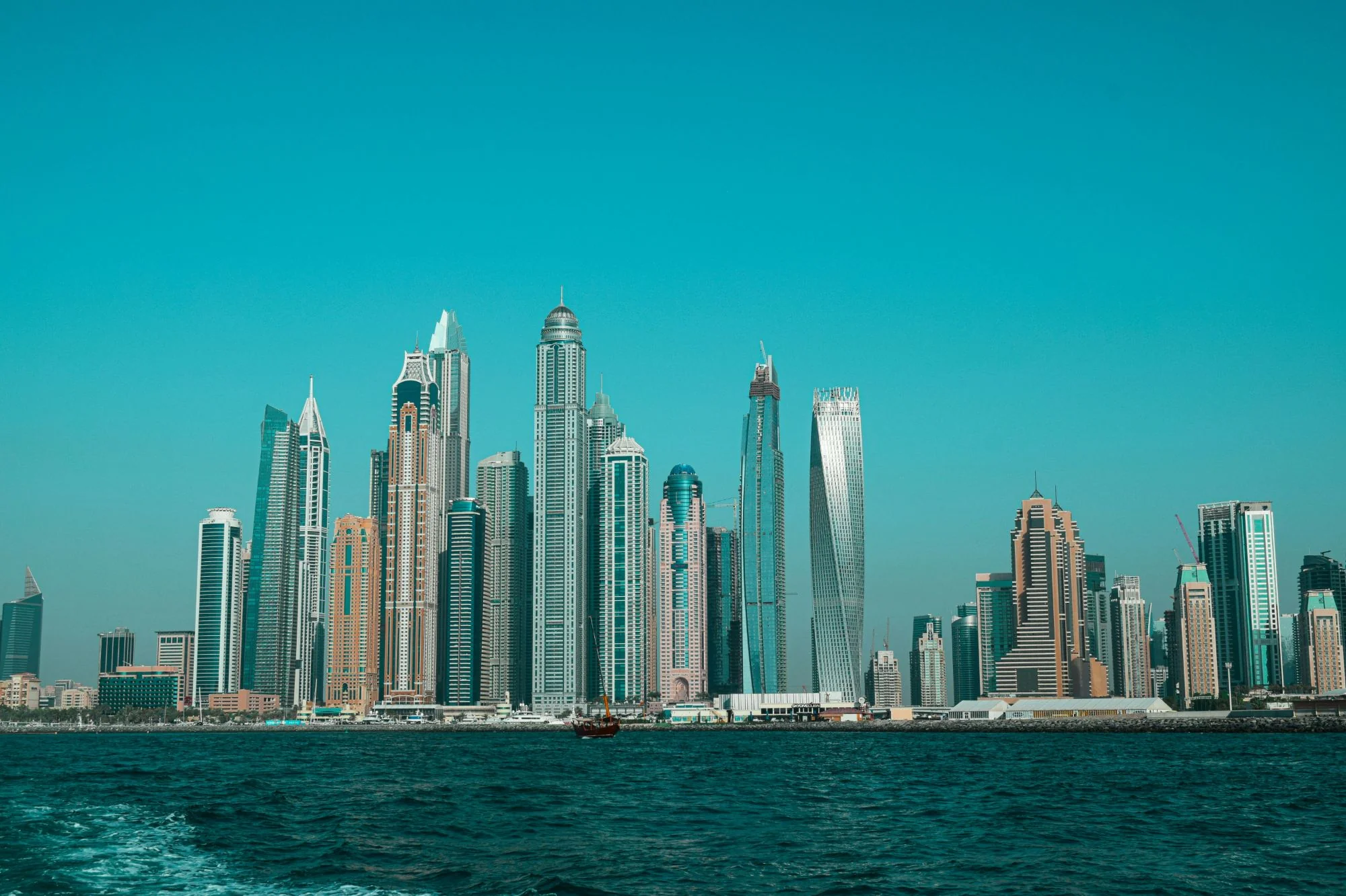 Skyline de Dubai Marina vu depuis l'eau, avec les tours de la marina sous un ciel bleu turquoise dégagé